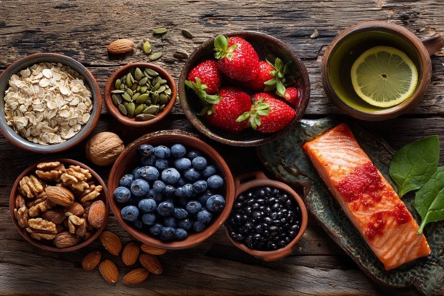 Vista de cima com aveia, frutas vermelhas, nozes, feijão, salmão e chá verde dispostos em uma bancada de cozinha.