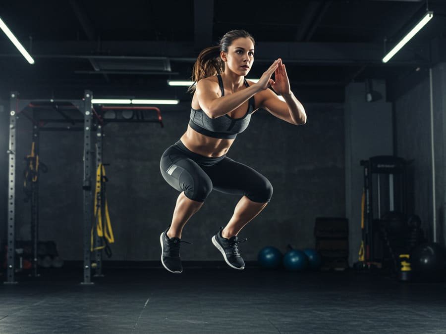 Melhor exercício para queimar gordura. Uma pessoa (com energia e determinação no rosto, mas ainda realista) no meio de um movimento dinâmico de alta intensidade, como um salto (box jump ou agachamento com salto)