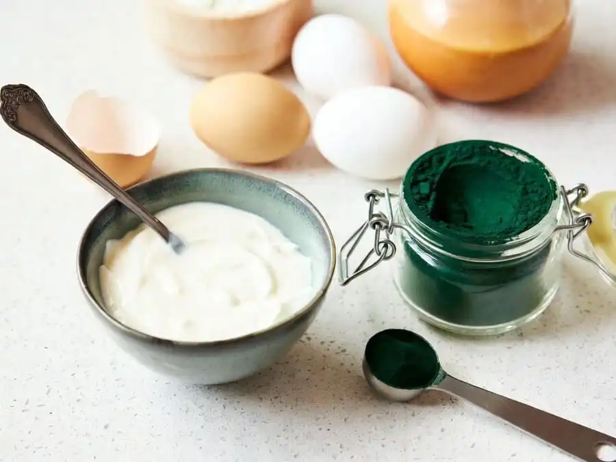 Ovos frescos, iogurte grego natural e spirulina em pó sobre bancada de cozinha, luz natural, destacando fontes de proteína de alto valor biológico.