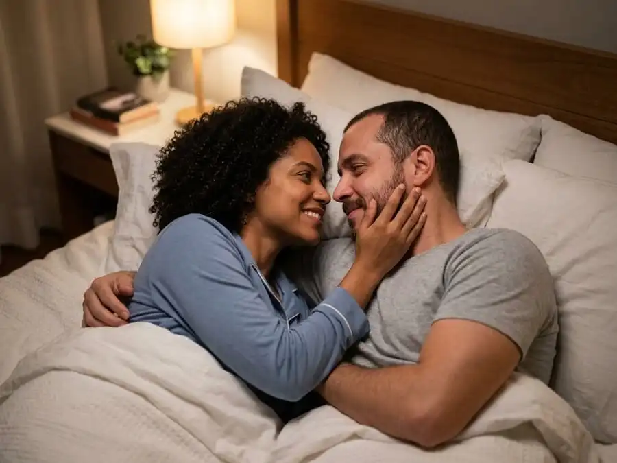 Casal deitado na cama se olhando e se tocando carinhosamente, simbolizando conexão e intimidade real no relacionamento.