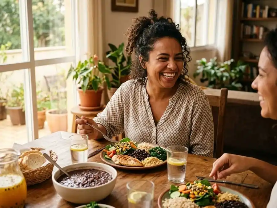 Pessoa sorrindo com bom humor após refeição equilibrada, mesa brasileira com luz natural suave, simbolizando controle da irritabilidade causada pela fome e benefícios de comer com calma.