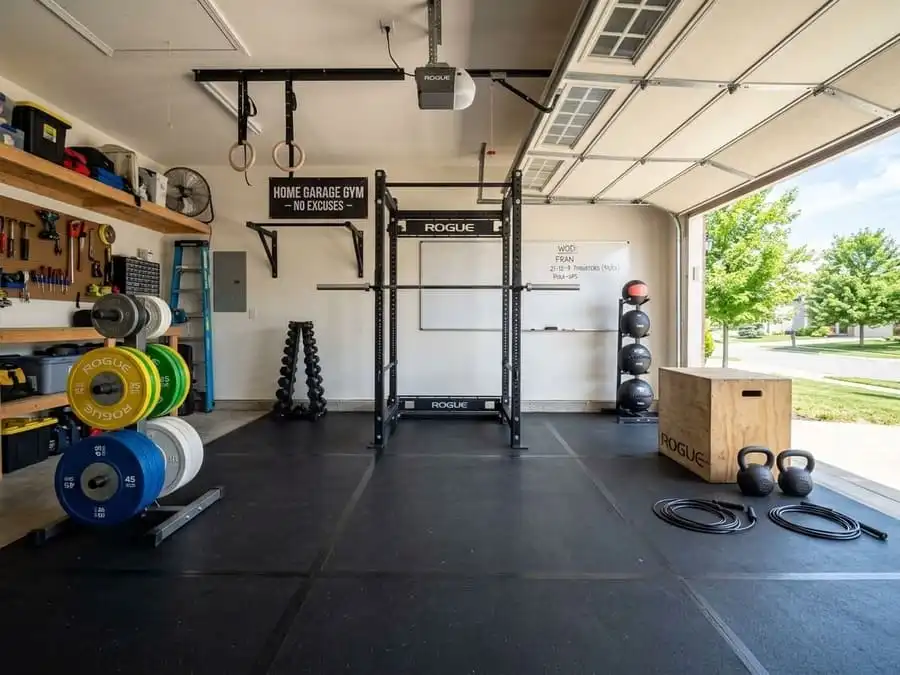 Espaço de treino funcional em uma garagem, com piso de borracha preta, rack de agachamento, barras, anilhas coloridas e acessórios de CrossFit organizados.