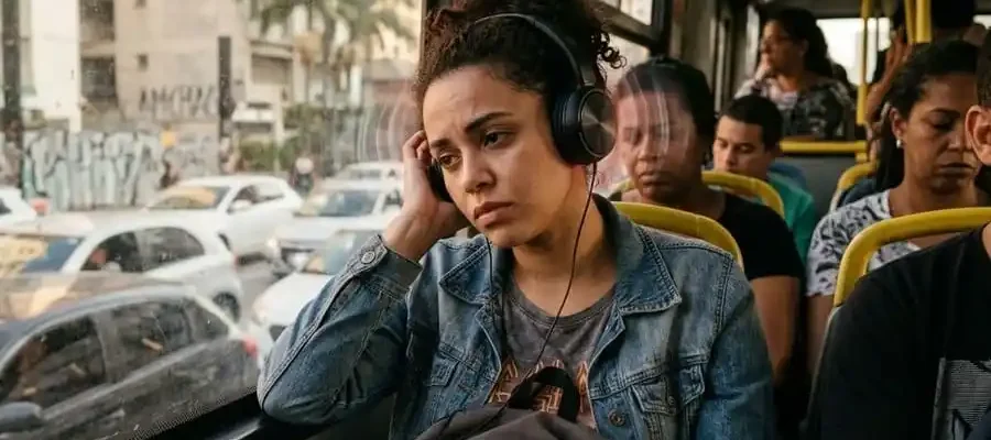 Pessoa usando fone de ouvido com expressão de desconforto, mão no ouvido, ambiente brasileiro cotidiano, luz natural ou de tela, simbolizando o risco cumulativo de uso prolongado e o sinal de alerta do tinnitus.