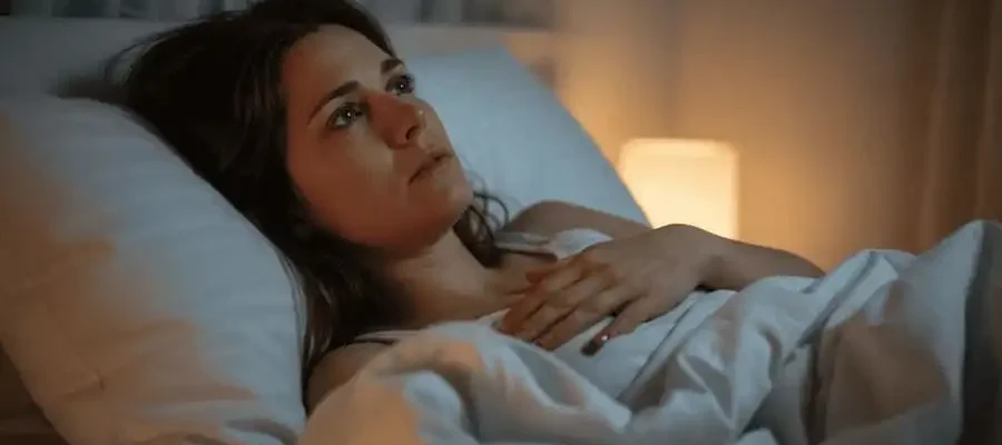 Mulher sozinha na cama à noite, expressão pensativa e melancólica, representando dúvida sobre os efeitos da abstinência sexual prolongada