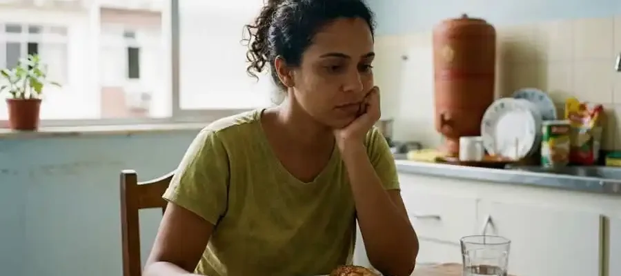 Pessoa sentada à mesa com expressão pensativa olhando para comida, luz natural suave em ambiente brasileiro, simbolizando o fenômeno do food noise e a obsessão alimentar constante.