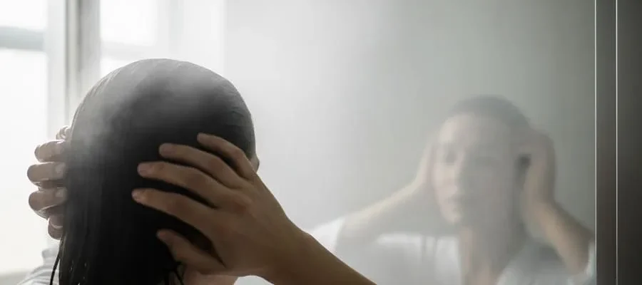 Pessoa de costas em frente a espelho embaçado de banheiro pós-banho, com luz natural suave entrando pela janela.