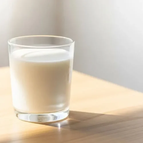 Imagem de uma pessoa adulta bebendo leite em uma cozinha moderna, com ilustrações sutis de ossos fortes ao fundo, simbolizando saúde óssea.